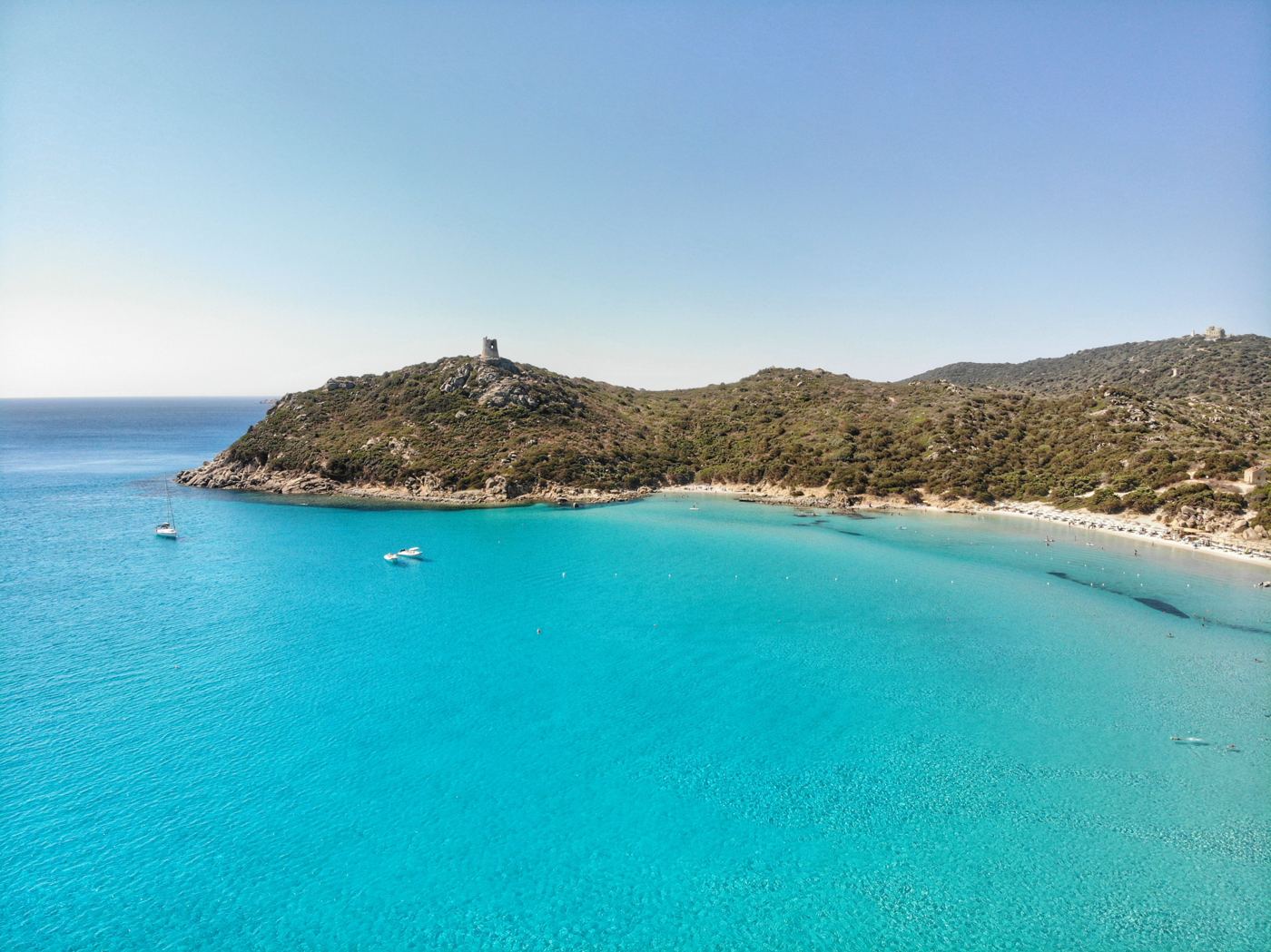 Turquoise bay in Sardinia below a hill with an old watchtower